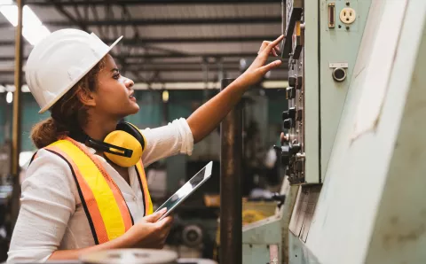 Female maintenance engineer inspecting relay protection system of machinery and holding digital tablet