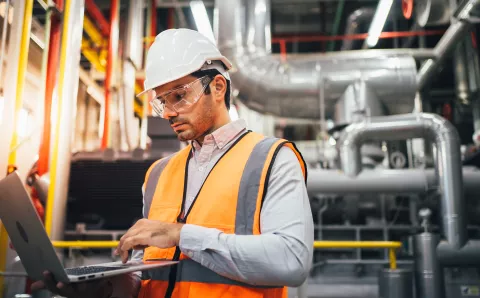 Professional worker of modern factory using laptop controlling program to automatic machinery.